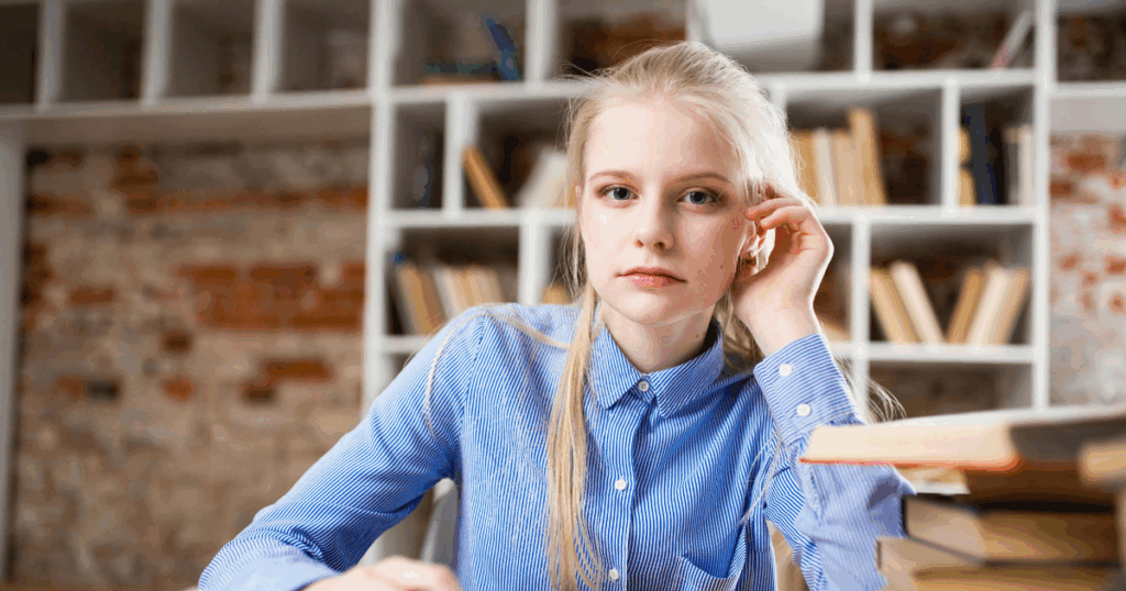 image - My Teen Mental Health Teen therapy: Young woman in blue shirt with books, bookshelf background, representing trust and communication in teen counseling.