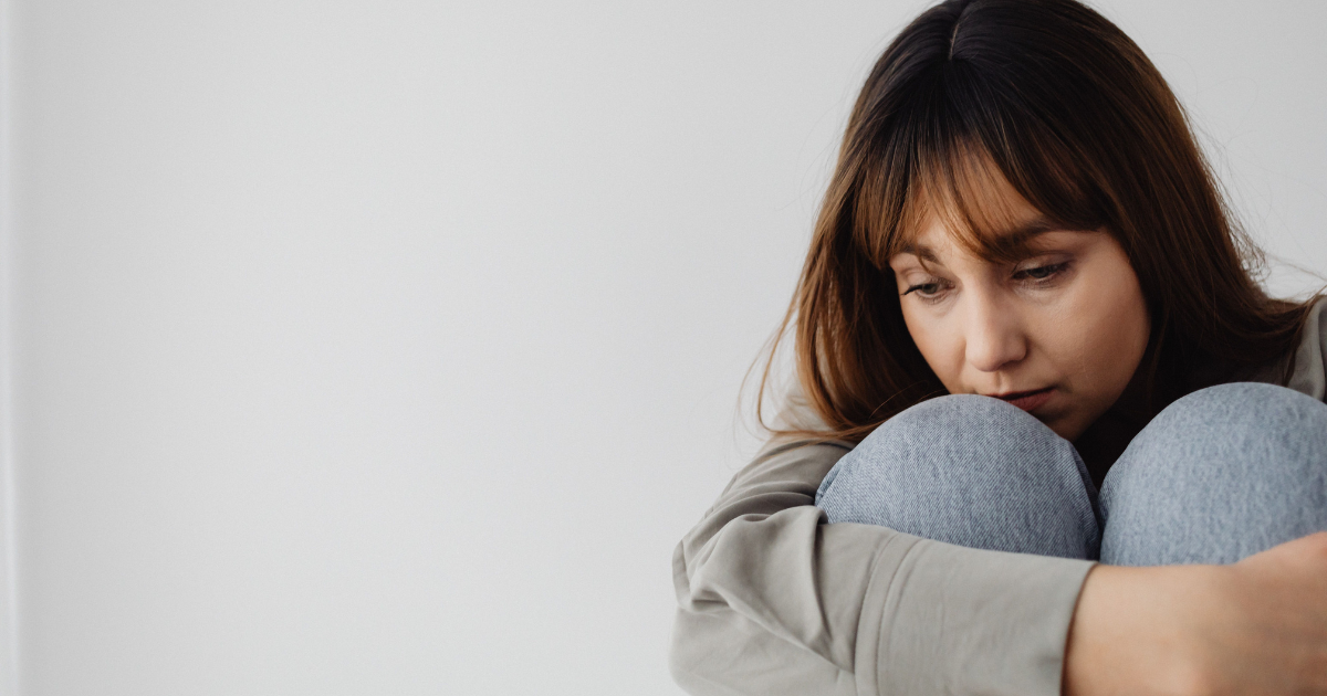 Woman sitting with knees drawn to her chest, looking down in a contemplative mood